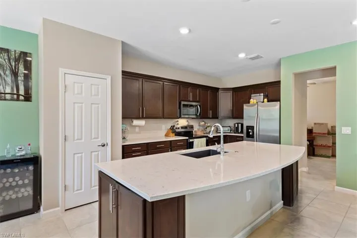 Kitchen featuring stainless steel appliances, dark brown cabinetry, light tile flooring, and a kitchen island with sink