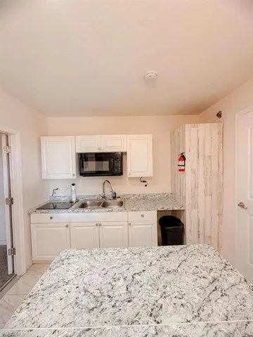 Kitchen featuring white cabinetry, black microwave, and light stone countertops