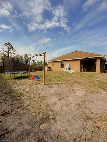 Rear view of property with a trampoline, a playground, and stucco siding