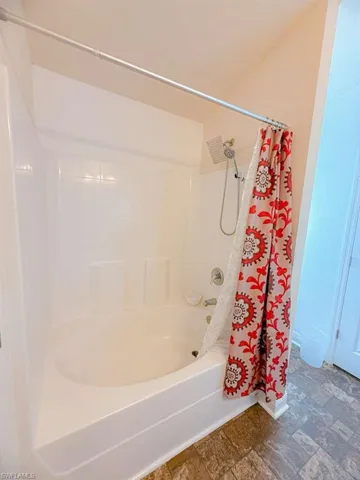 Full bath with stone finish floors and shower / bath combination with curtain