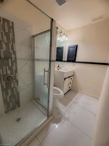 Full bathroom with vanity, a textured wall, a shower stall, and light marble finish flooring