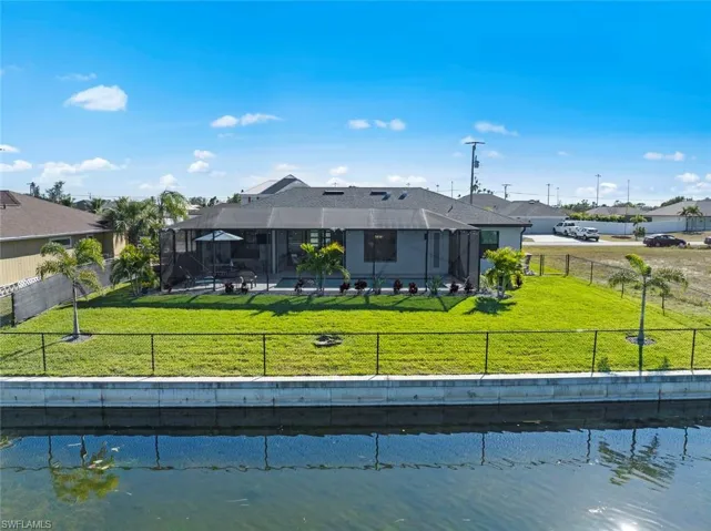 Back of property featuring a lawn, a water view, and a lanai