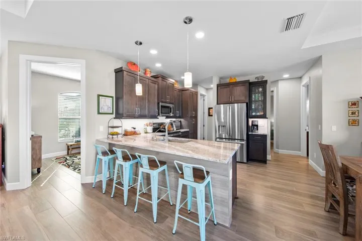 Kitchen featuring kitchen peninsula, a kitchen breakfast bar, dark brown cabinets, stainless steel appliances, and decorative light fixtures