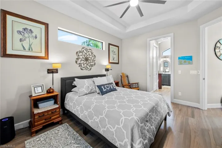 Bedroom featuring a raised ceiling, ensuite bathroom, hardwood / wood-style floors, and ceiling fan