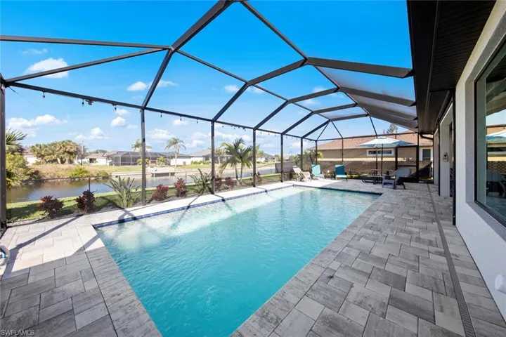 View of pool featuring glass enclosure, a patio area, and a water view
