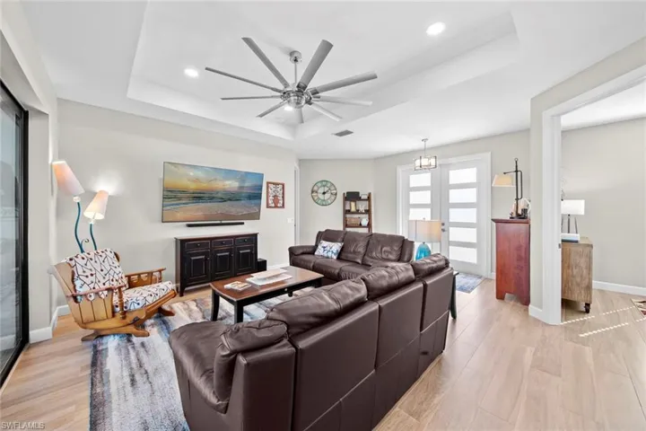 Living room featuring ceiling fan with notable chandelier, light hardwood / wood-style flooring, and a tray ceiling
