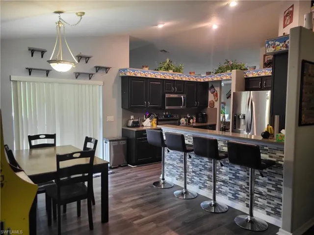 Kitchen with high vaulted ceiling, wood-type flooring, decorative light fixtures, and appliances with stainless steel finishes