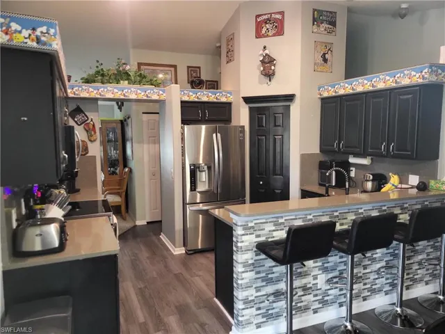 Kitchen with dark wood-type flooring, stainless steel fridge, kitchen peninsula, a breakfast bar, and tasteful backsplash