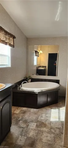 Full bath with vanity, a garden tub, wallpapered walls, and light stone finish flooring