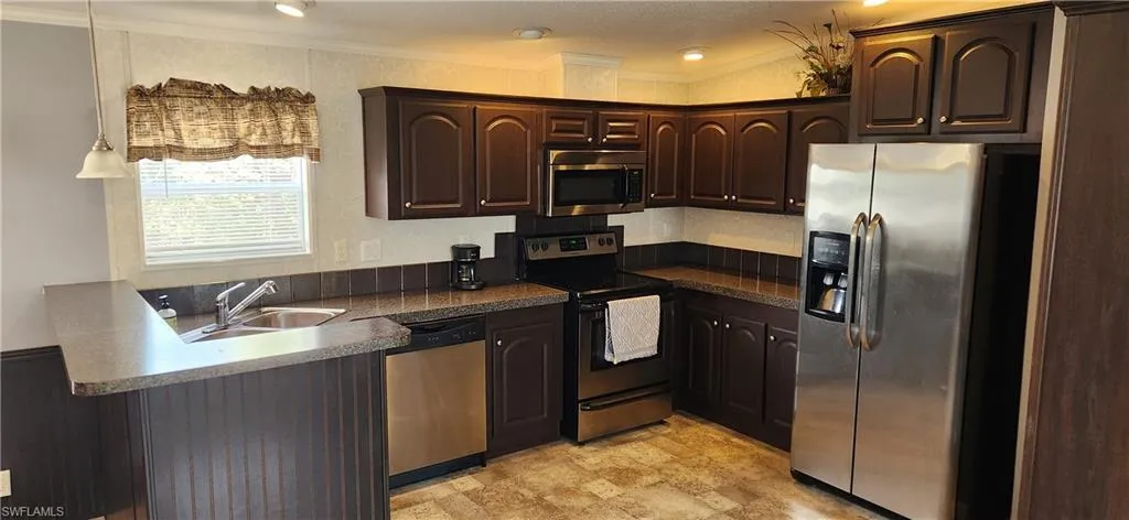 Kitchen featuring dark brown cabinets, stainless steel appliances, a peninsula, dark countertops, and ornamental molding