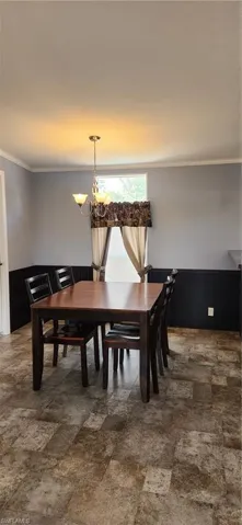 Dining room with wainscoting, crown molding, a chandelier, wooden walls, and stone finish flooring