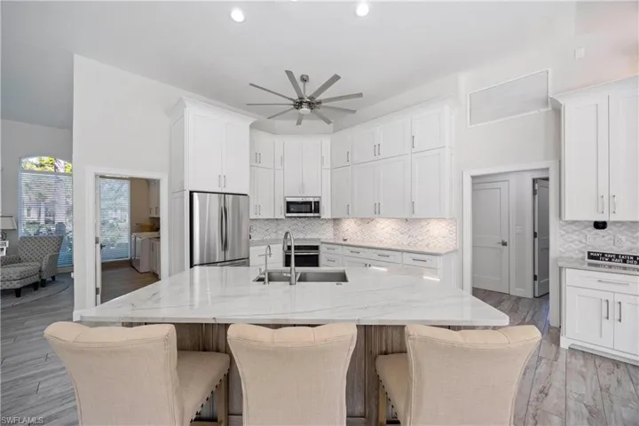 Kitchen featuring light stone counters, stainless steel appliances, white cabinets, a sink, and a ceiling fan