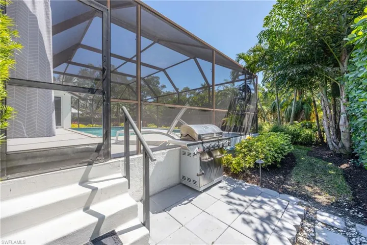 View of patio featuring glass enclosure, an outdoor pool, an outdoor kitchen, and a grill