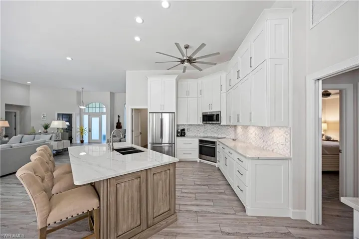 Kitchen featuring decorative backsplash, a sink, stainless steel appliances, open floor plan, and a ceiling fan