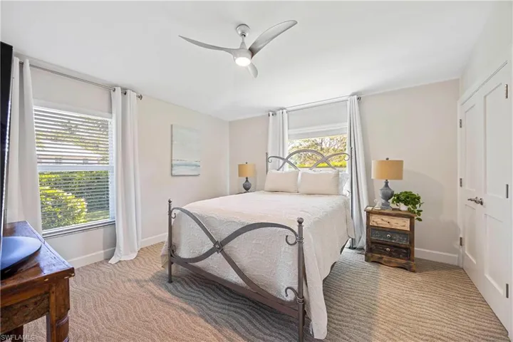 Carpeted bedroom with a ceiling fan, multiple windows, and baseboards