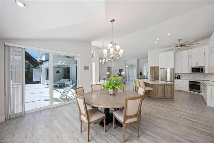 Dining area with lofted ceiling, recessed lighting, light wood finished floors, and ceiling fan with notable chandelier