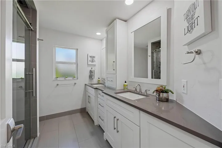 Full bath featuring baseboards, an enclosed shower, double vanity, and a sink