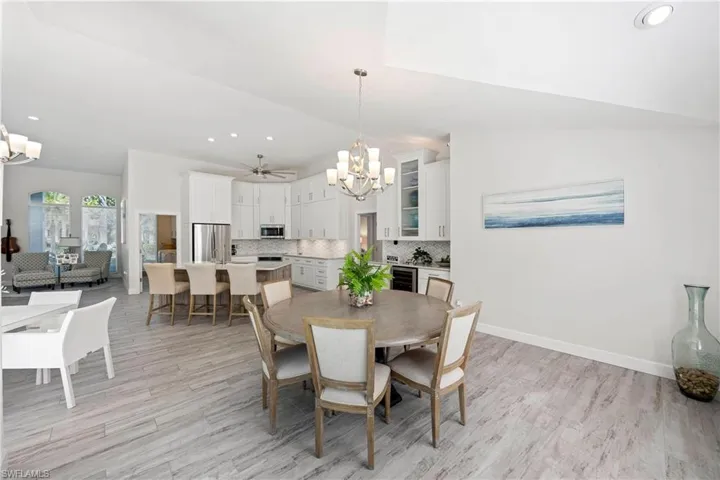 Dining area featuring lofted ceiling, light wood-style flooring, recessed lighting, wine cooler, and ceiling fan with notable chandelier