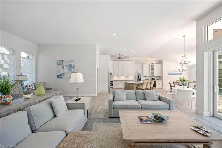 Living area featuring ceiling fan with notable chandelier, baseboards, and light wood-style floors
