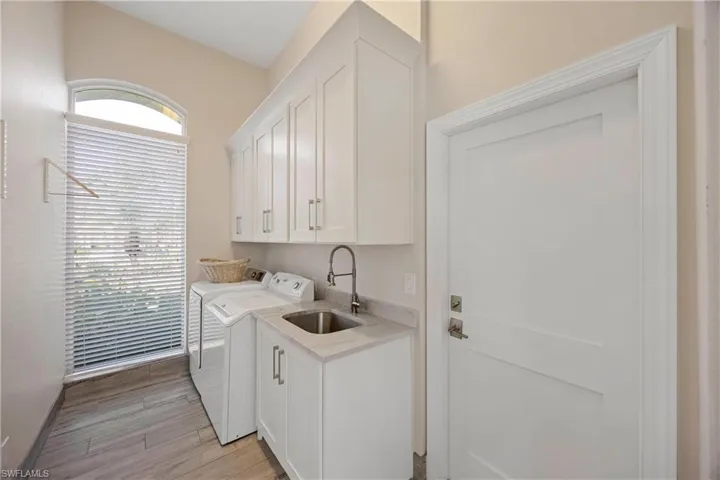 Laundry area featuring light wood-style flooring, a sink, washing machine and clothes dryer, and cabinet space