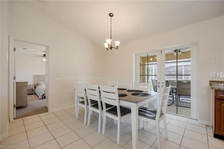 Dining space with light tile patterned floors, vaulted ceiling, and ceiling fan with notable chandelier