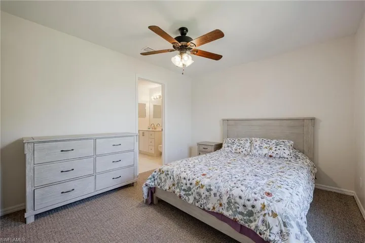 Carpeted bedroom featuring ensuite bath and ceiling fan