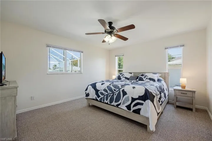 Carpeted bedroom with ceiling fan and multiple windows