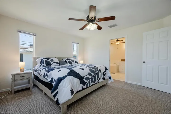 Carpeted bedroom featuring ensuite bath and ceiling fan