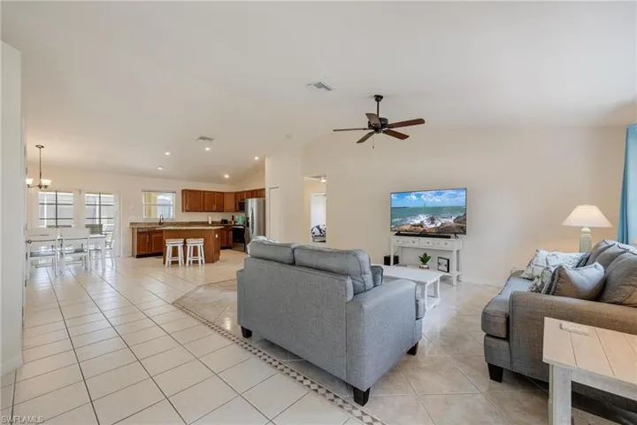 Living room featuring light tile patterned floors, sink, ceiling fan with notable chandelier, and lofted ceiling