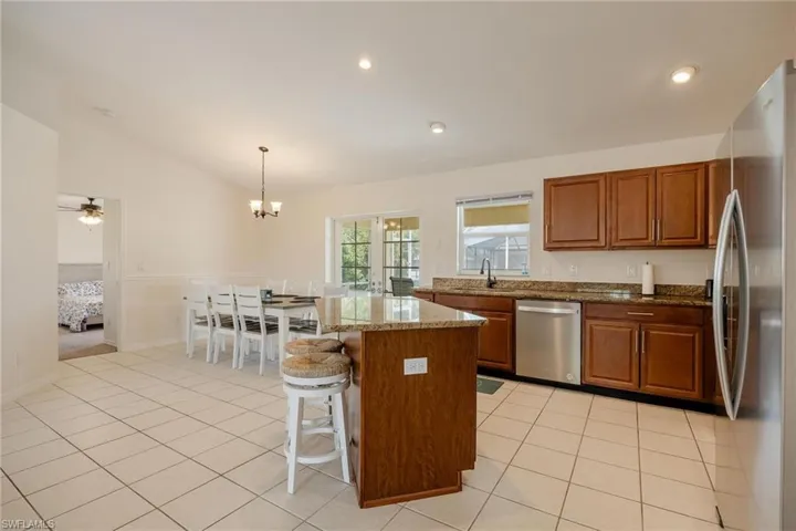 Kitchen featuring a center island, ceiling fan with notable chandelier, appliances with stainless steel finishes, lofted ceiling, and pendant lighting
