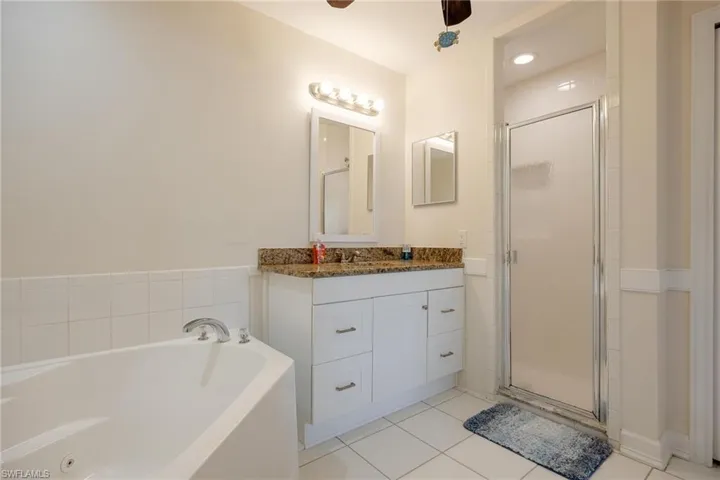 Bathroom with tile patterned floors, ceiling fan, separate shower and tub, and vanity