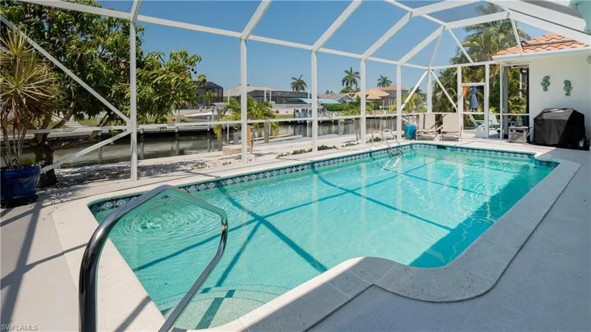 View of swimming pool with area for grilling, a water view, a patio, and glass enclosure