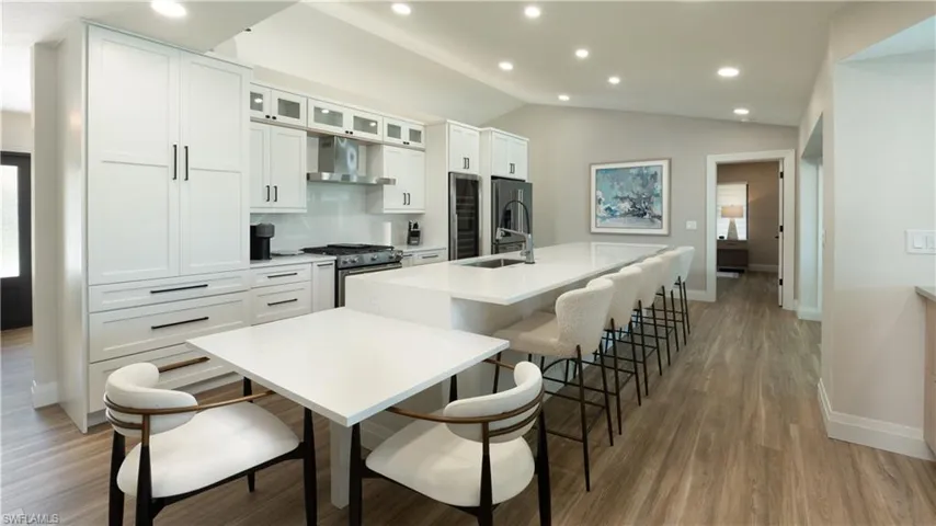 Kitchen featuring sink, stainless steel appliances, wall chimney range hood, a kitchen island with sink, and white cabinets