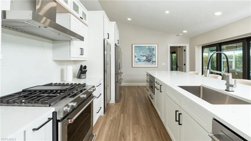 Kitchen featuring light stone countertops, wall chimney exhaust hood, stainless steel appliances, sink, and white cabinets