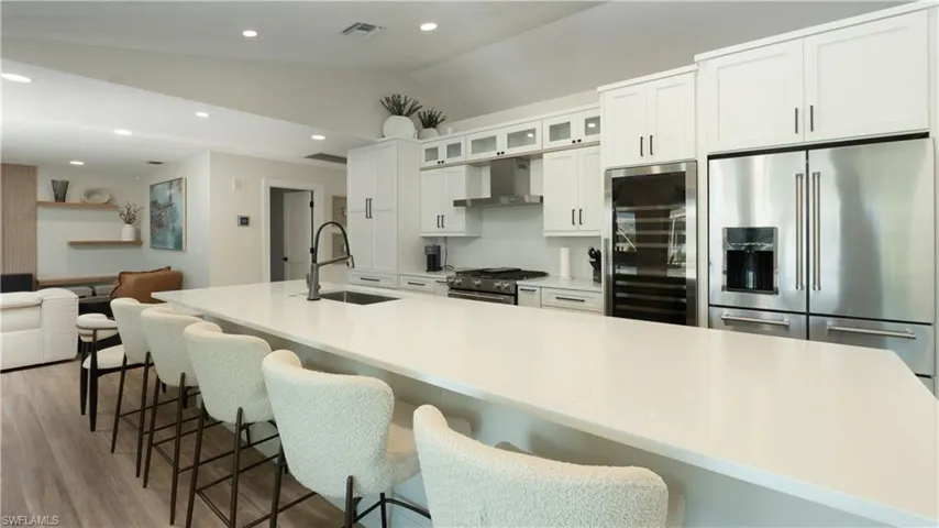 Kitchen with white cabinetry, sink, wall chimney exhaust hood, stainless steel appliances, and vaulted ceiling