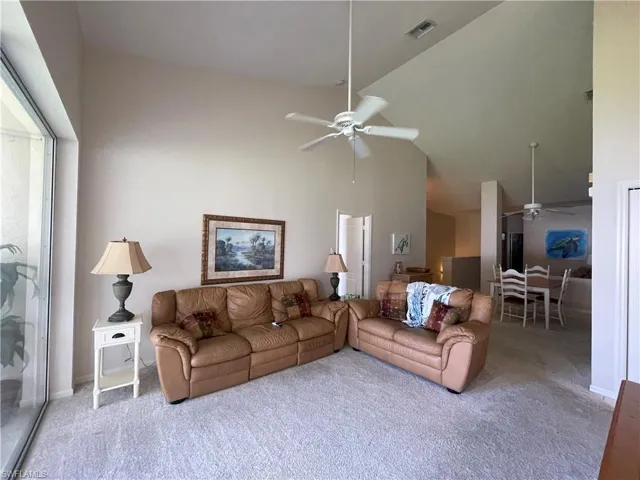 Living room featuring a ceiling fan, carpet flooring, and lofted ceiling