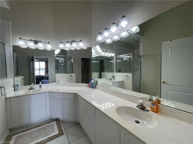 Bathroom featuring light tile patterned floors, double vanity, a stall shower, a high ceiling, and ensuite bath