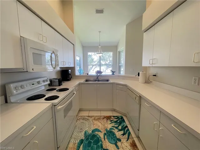 Kitchen featuring white appliances, light countertops, decorative light fixtures, light tile patterned floors, and white cabinetry