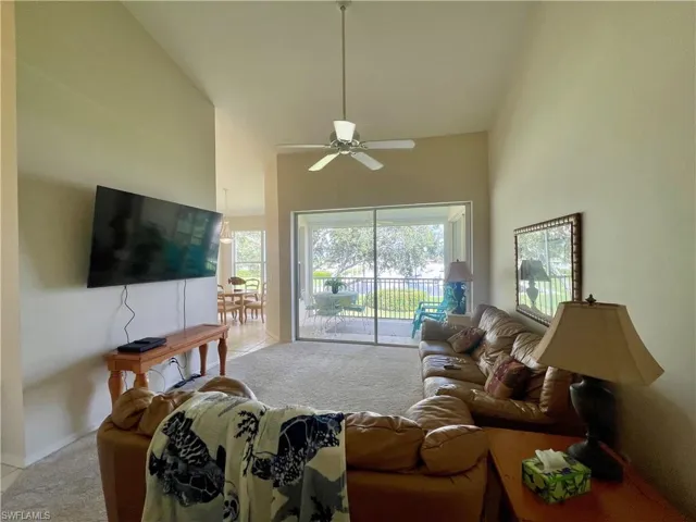 Living room with light colored carpet, a ceiling fan, and vaulted ceiling