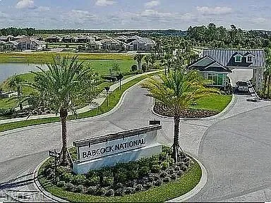 Entryway featuring a large sign, mature palm trees, and manicured landscaping