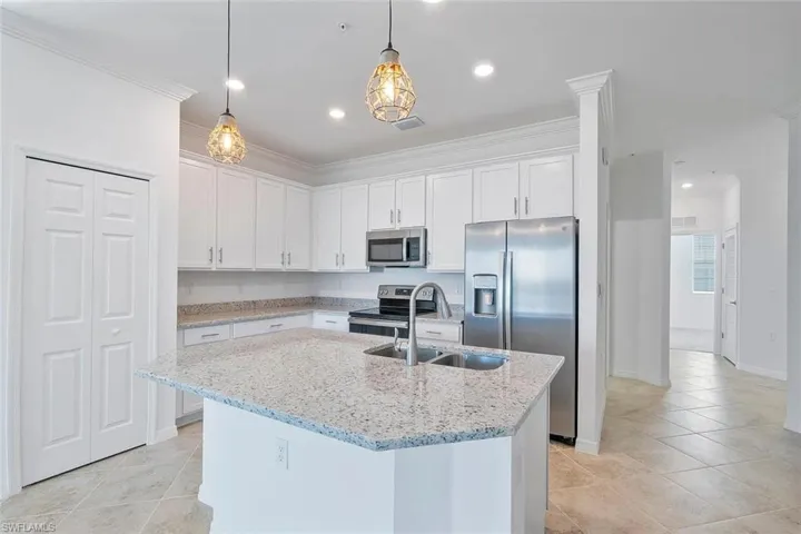 Kitchen featuring an island with a double basin sink, white cabinetry, integrated stainless steel appliances, and tile flooring