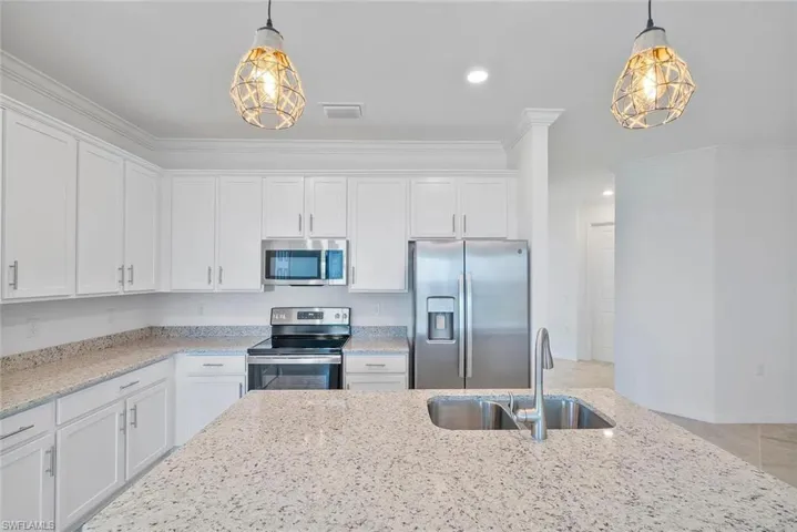 Kitchen featuring white cabinetry, stainless steel appliances, speckled countertops, a double basin sink, and decorative pendant lighting