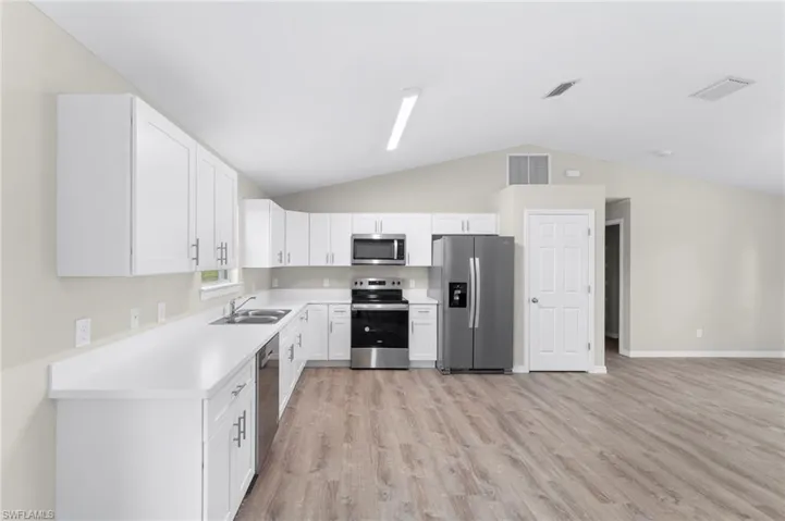 Kitchen with white cabinetry, sink, light hardwood / wood-style flooring, vaulted ceiling, and appliances with stainless steel finishes