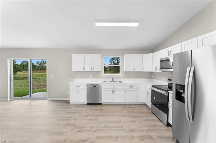 Kitchen with white cabinets, light wood-type flooring, stainless steel appliances, and vaulted ceiling