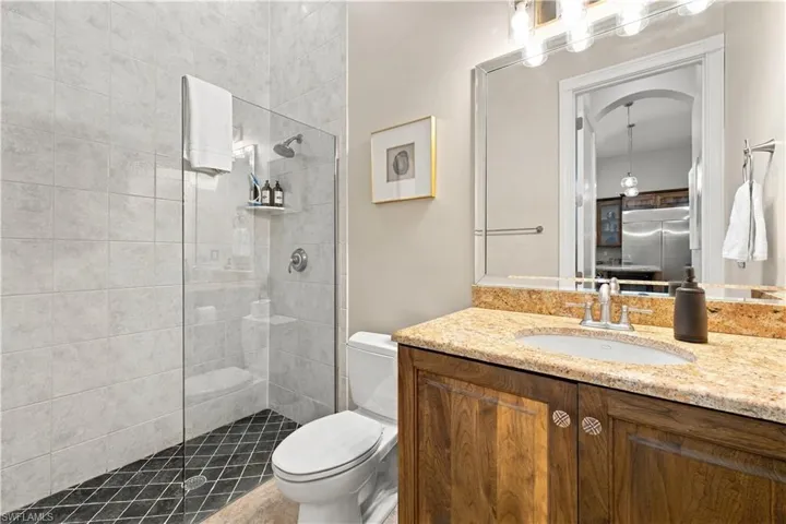 Bathroom featuring a walk-in shower with glass enclosure, custom wood cabinetry, stone-finish countertop, undermount sink, and large wall-mounted mirror
