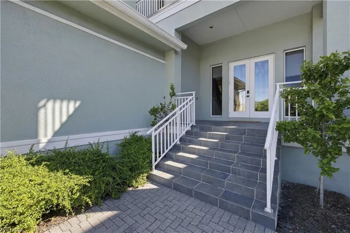 Entrance featuring stone-tiled steps, white metal handrails, a double-door entryway, and paver hardscaping