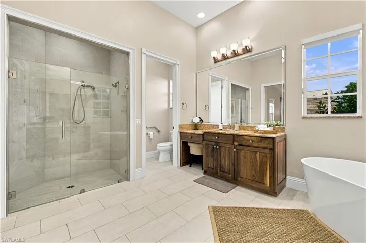 Walk-in shower with floor-to-ceiling tile, freestanding soaking tub, custom wood cabinetry, stone-finish countertop, and large wall-mounted mirror