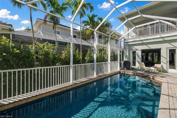 Screen-enclosed swimming pool featuring a paver deck, white metal railing, and exterior wall-mounted lighting