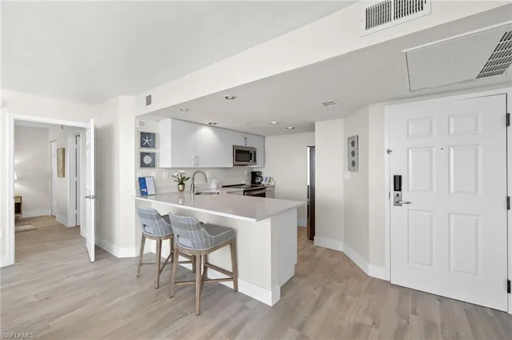 Kitchen featuring kitchen peninsula, appliances with stainless steel finishes, a kitchen bar, sink, and white cabinets