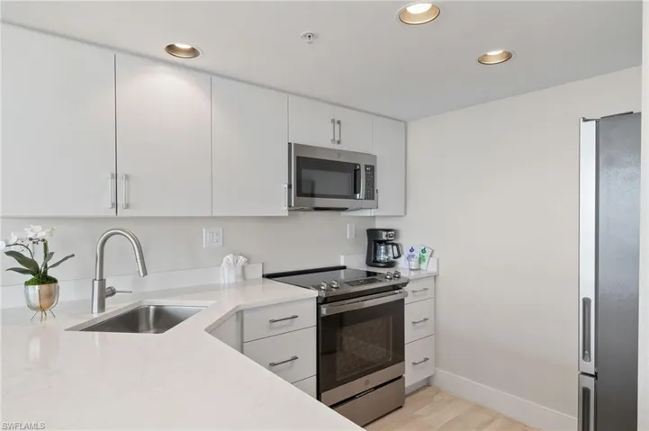 Kitchen featuring white cabinets, sink, light stone countertops, light hardwood / wood-style floors, and stainless steel appliances